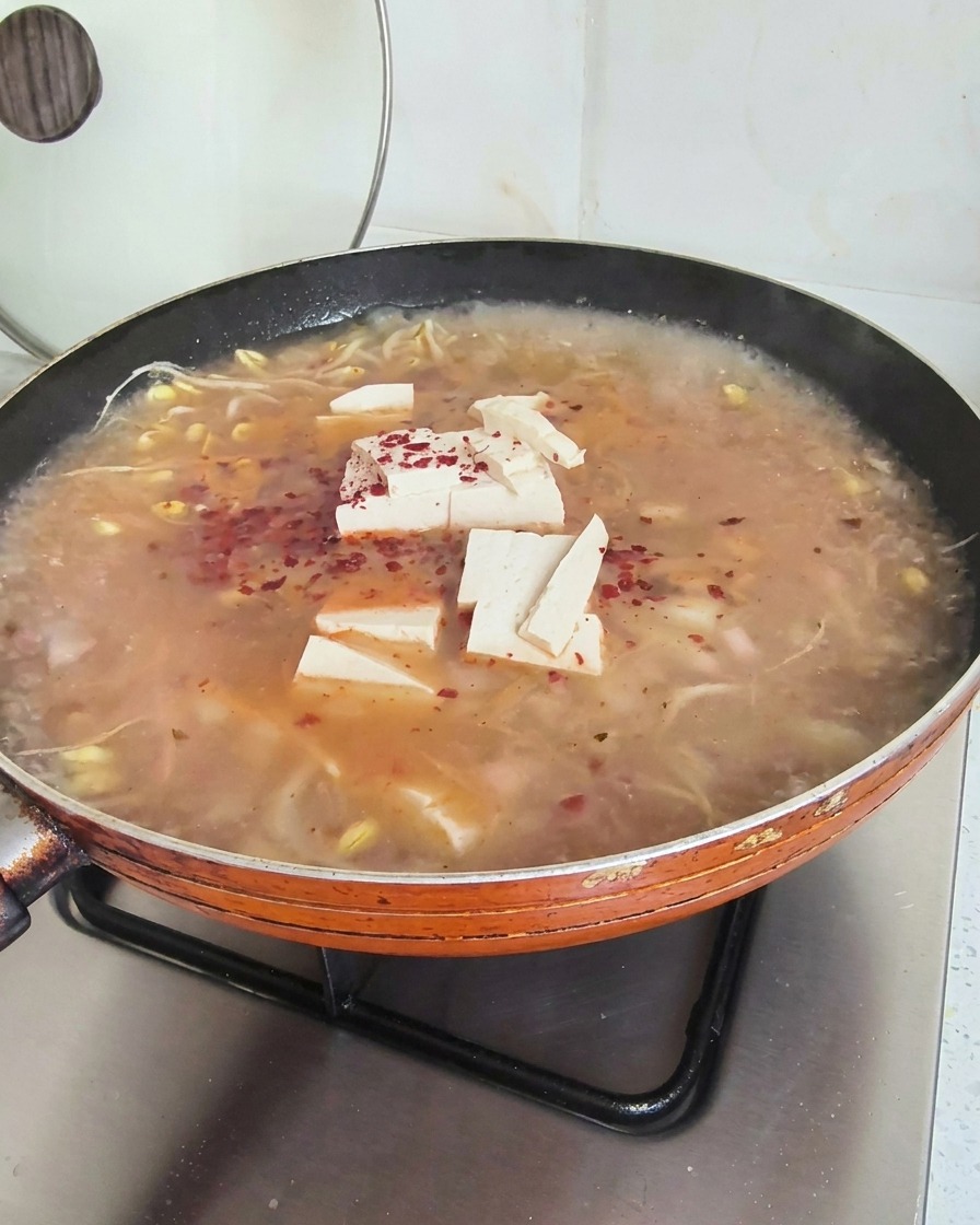 Fiocchi di peperoncino rosso brillante sparsi sopra una zuppa fumante con tofu e germogli di soia.