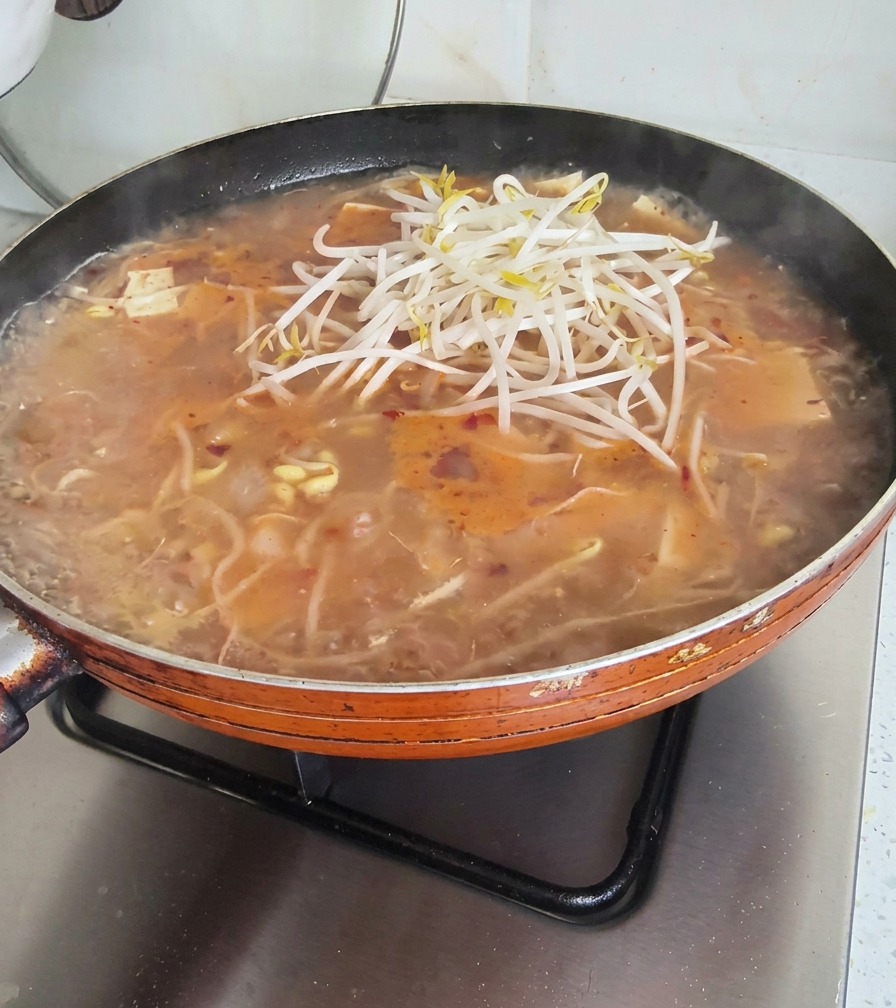 Una generosa manciata di germogli di soia freschi posizionata sopra una padella di zuppa bollente.