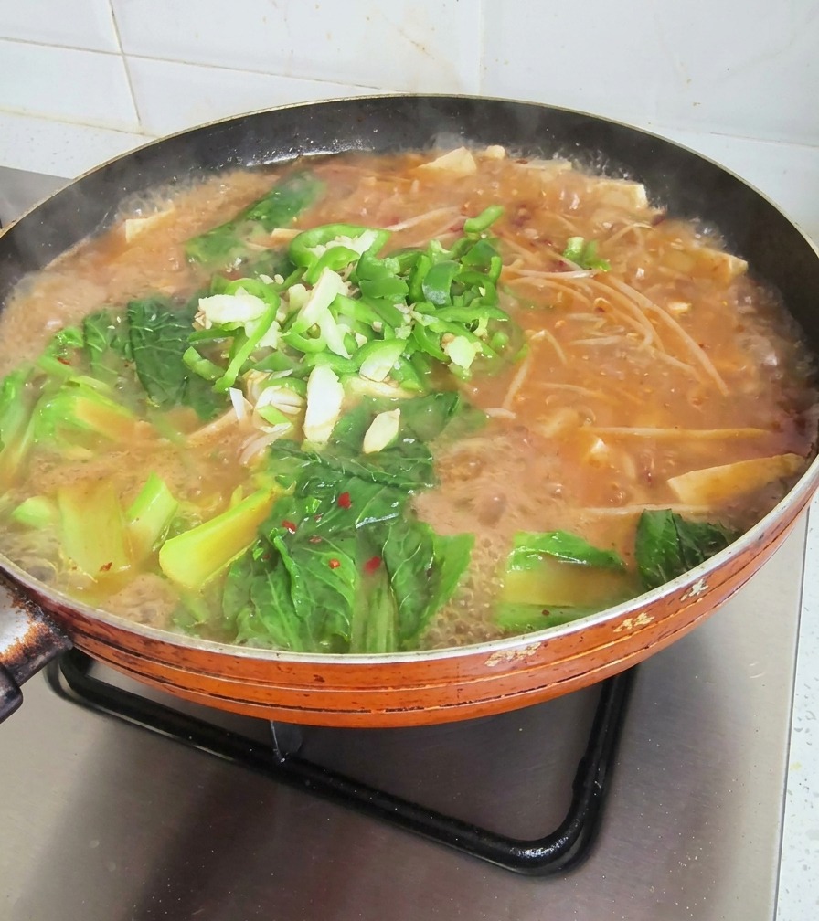 Padella bollente di zuppa coreana guarnita con verdure fresche, peperoncini affettati e aglio tritato.