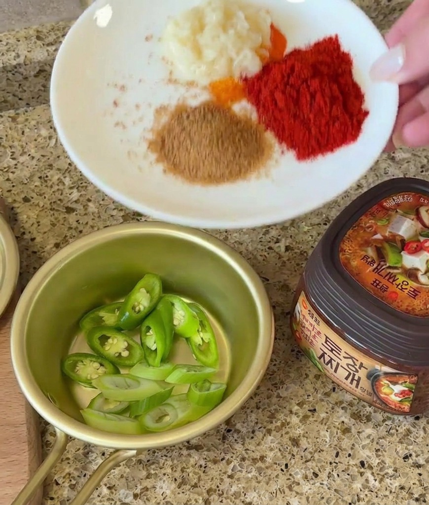 Una mano tiene un piatto con aglio e spezie accanto a peperoncini affettati e un barattolo di pasta di soia.