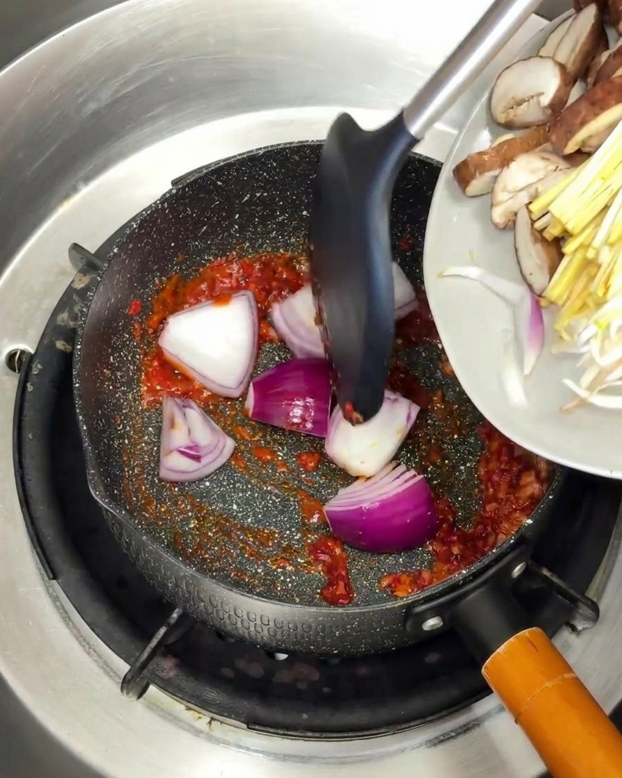 Cipolla rossa e funghi affettati aggiunti alla base di spezie rosse in padella.