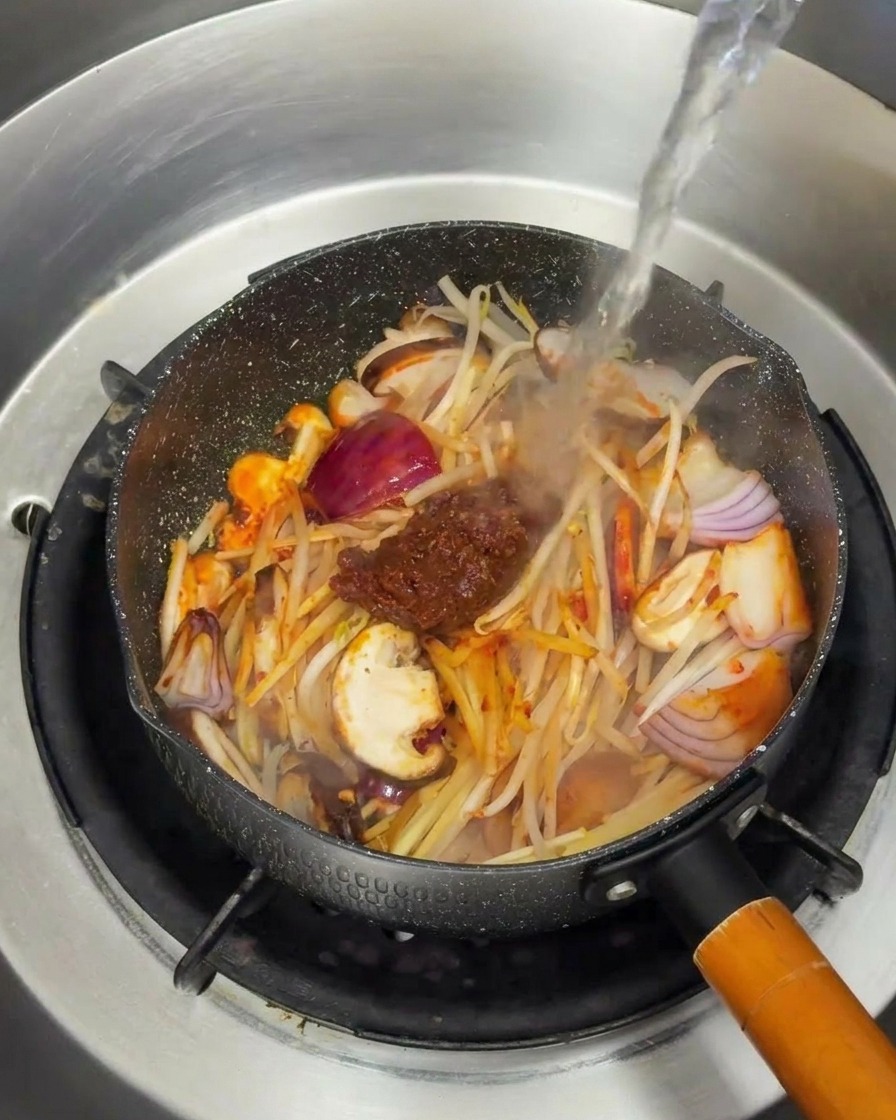 Acqua bollente versata sulle verdure saltate e la pasta di soia.