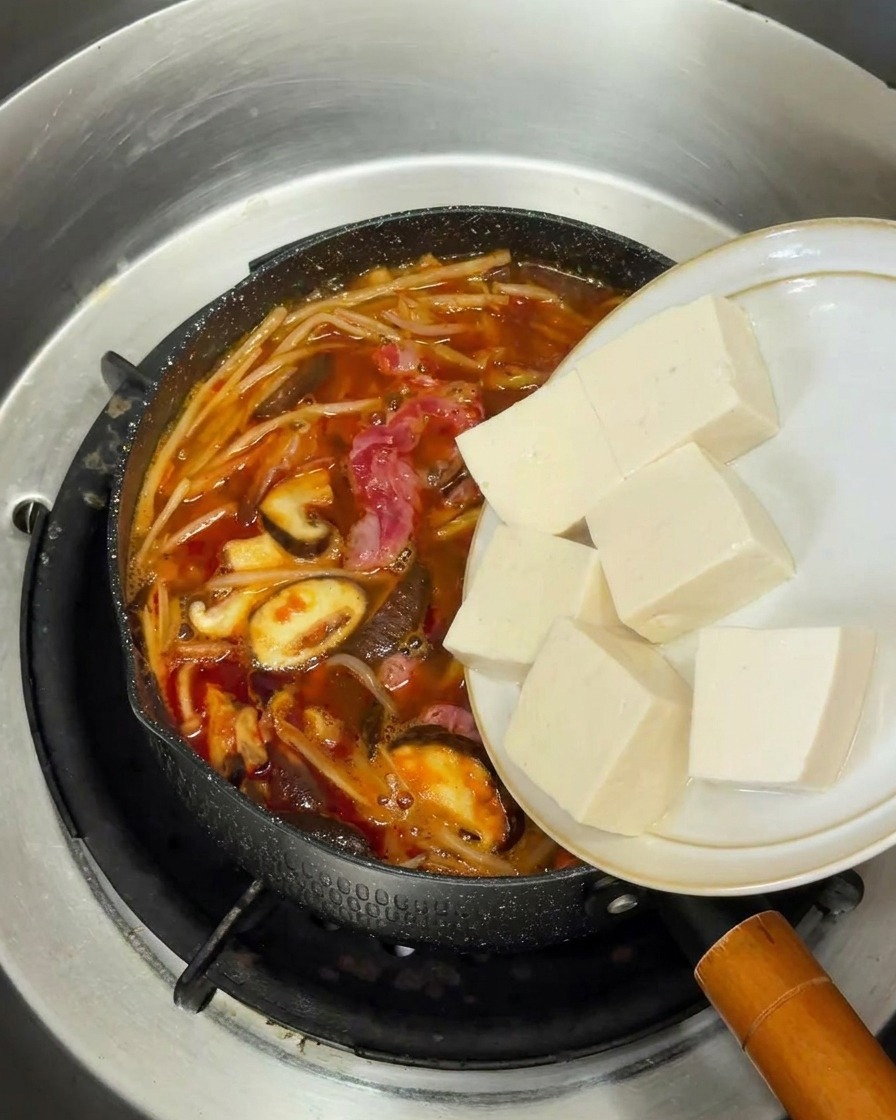 Cubetti di tofu bianco aggiunti alla zuppa di manzo coreana in ebollizione.