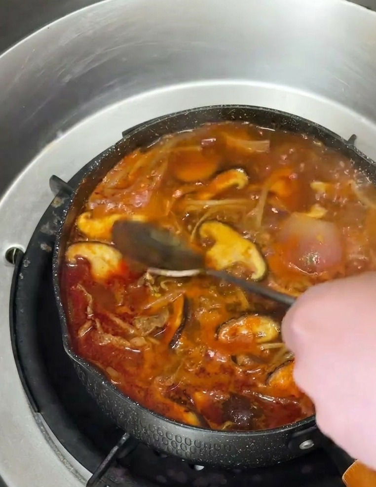 Un cucchiaio versa olio di sesamo ambrato nella zuppa piccante con funghi.