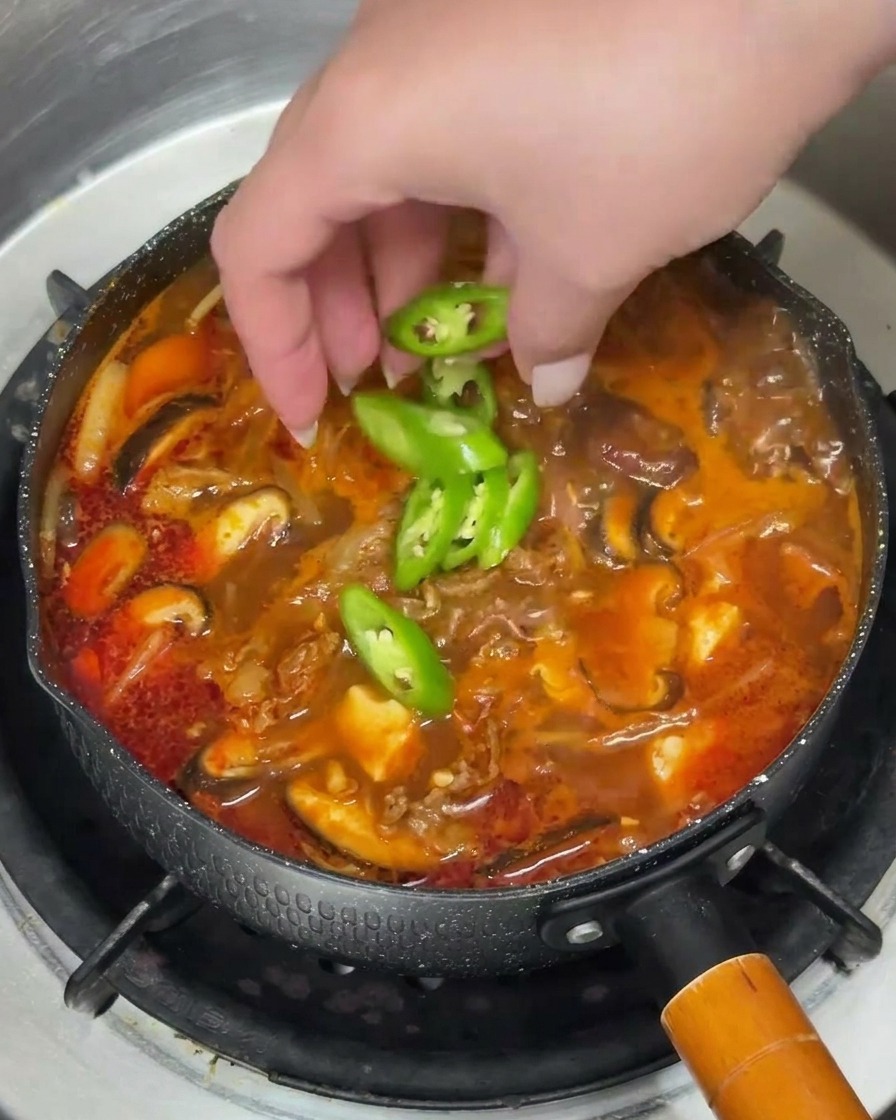 Mano che distribuisce peperoncini verdi e cipollotti tritati sulla zuppa fumante.