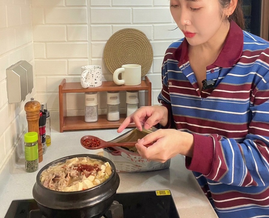 Un cucchiaio di legno che aggiunge peperoncino rosso in polvere a uno stufato con carne, tofu e zucchine