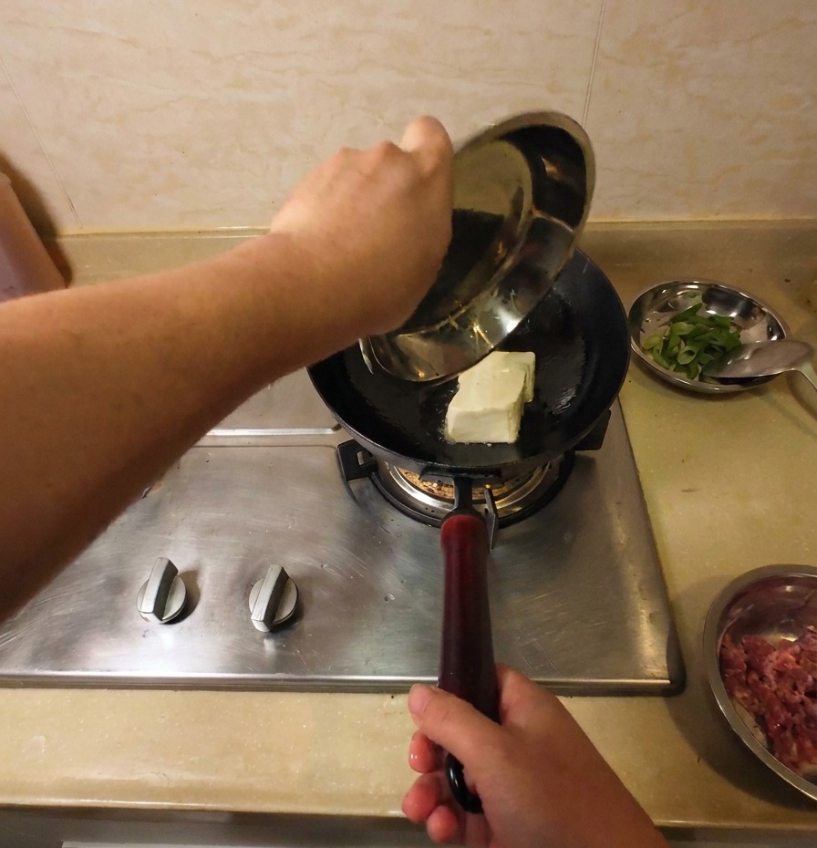 Un intero blocco di tofu bianco viene immerso nel wok con lolio caldo per iniziare la frittura.