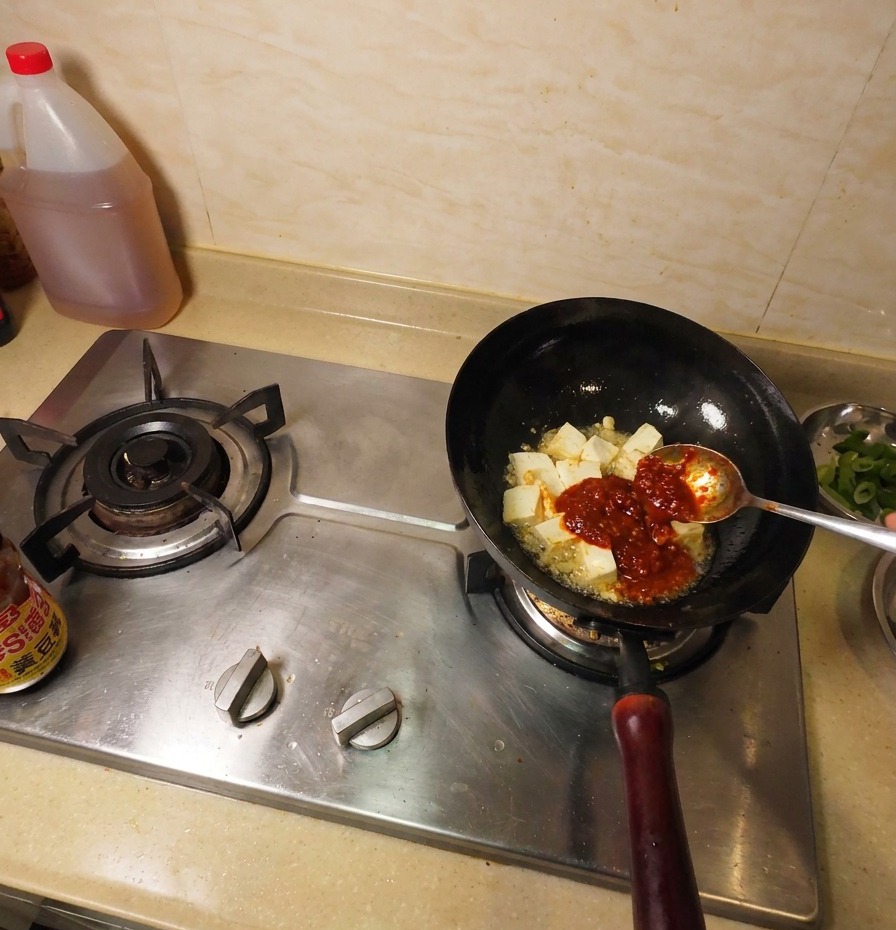 Pasta di soia marrone scuro aggiunta al wok insieme al tofu fritto e alla salsa rossa.