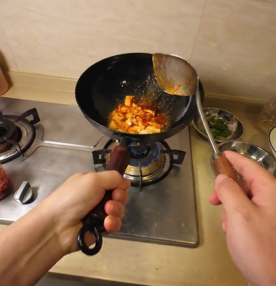 Pezzi di tofu saltati e rivestiti da una saporita salsa rossa in un wok nero.