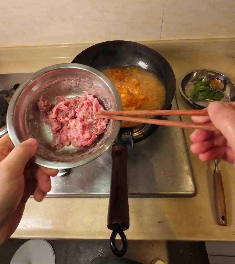 Una mano usa le bacchette per immergere sottili fette di manzo infarinate in una zuppa che bolle.