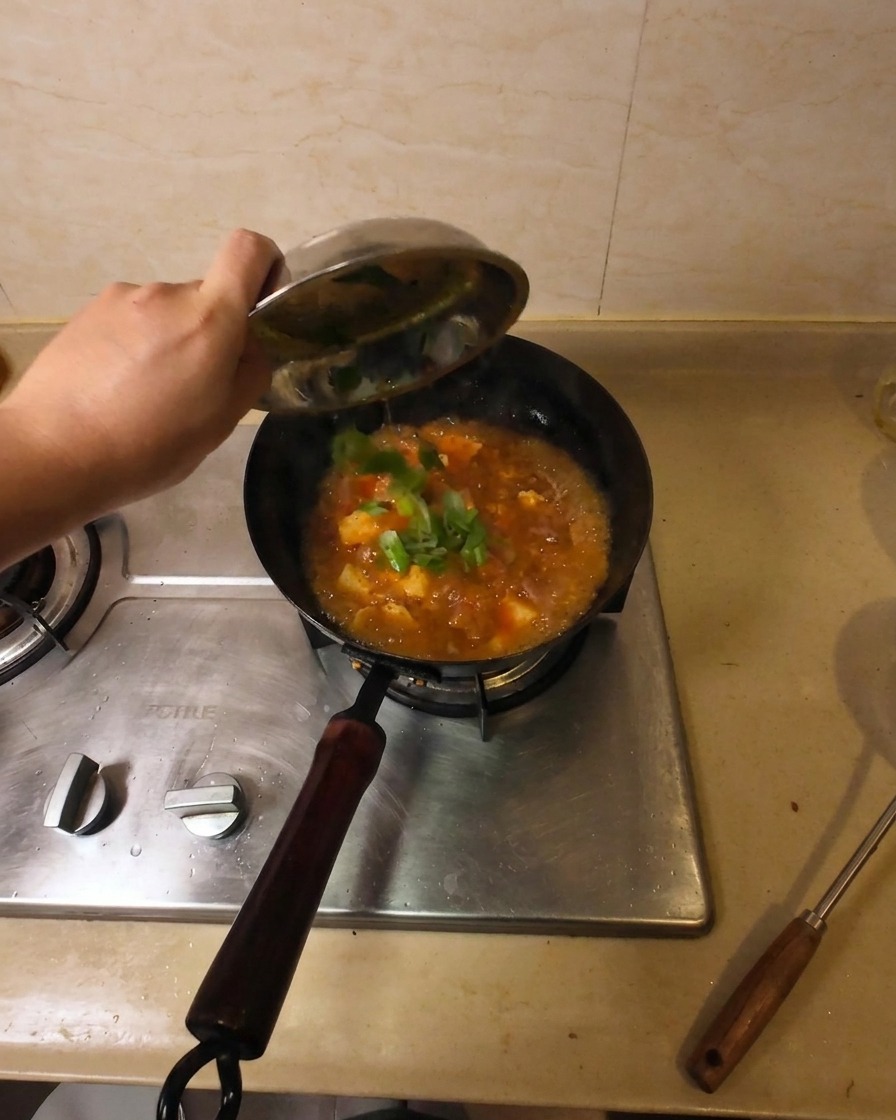 Una mano versa cipollotti freschi tritati da una ciotolina in un wok con la zuppa di manzo e tofu.