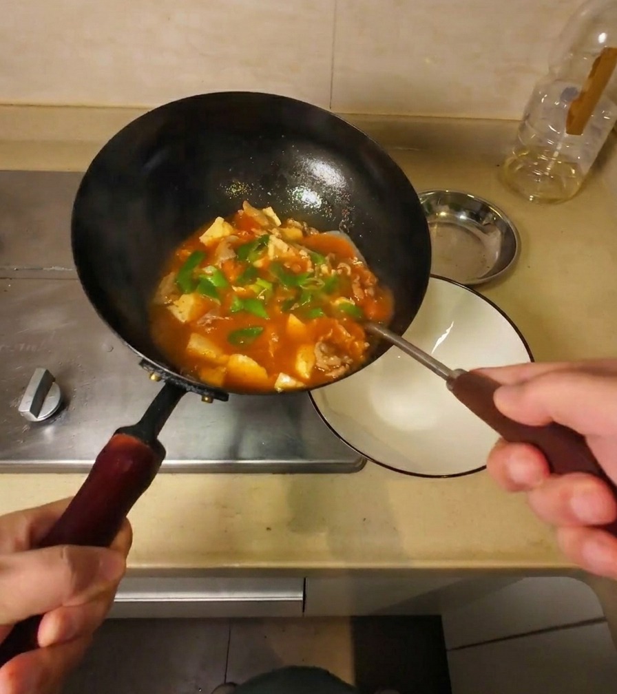 Zuppa densa di manzo e tofu versata da un wok nero in una ciotola di ceramica bianca.