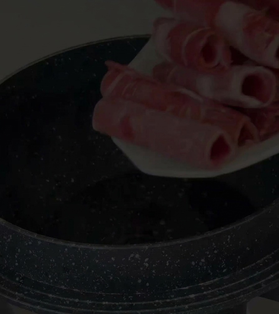 Una mano che mette sottili fette di punta di petto di manzo cruda in una pentola antiaderente nera.
