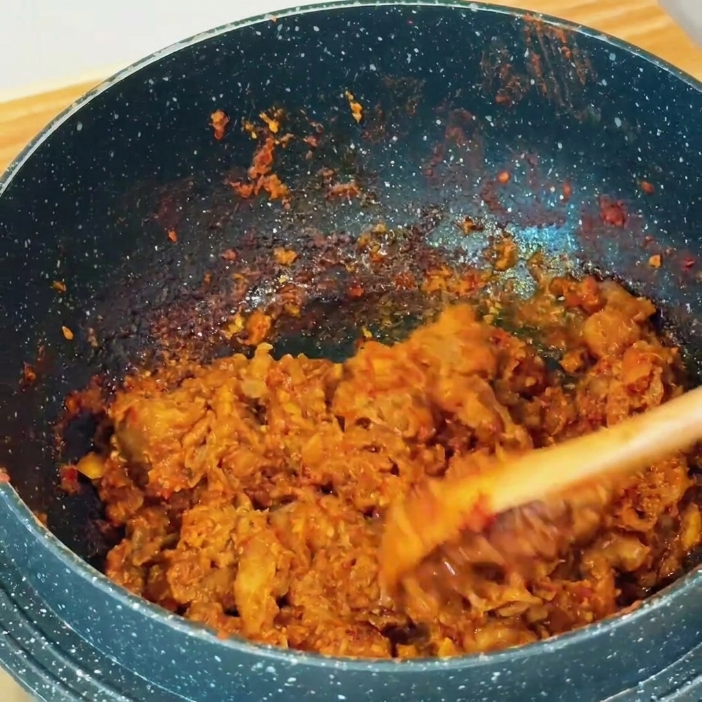 Sottili fette di manzo saltate con pasta di soia bruna in una pentola scura usando una spatola di legno.