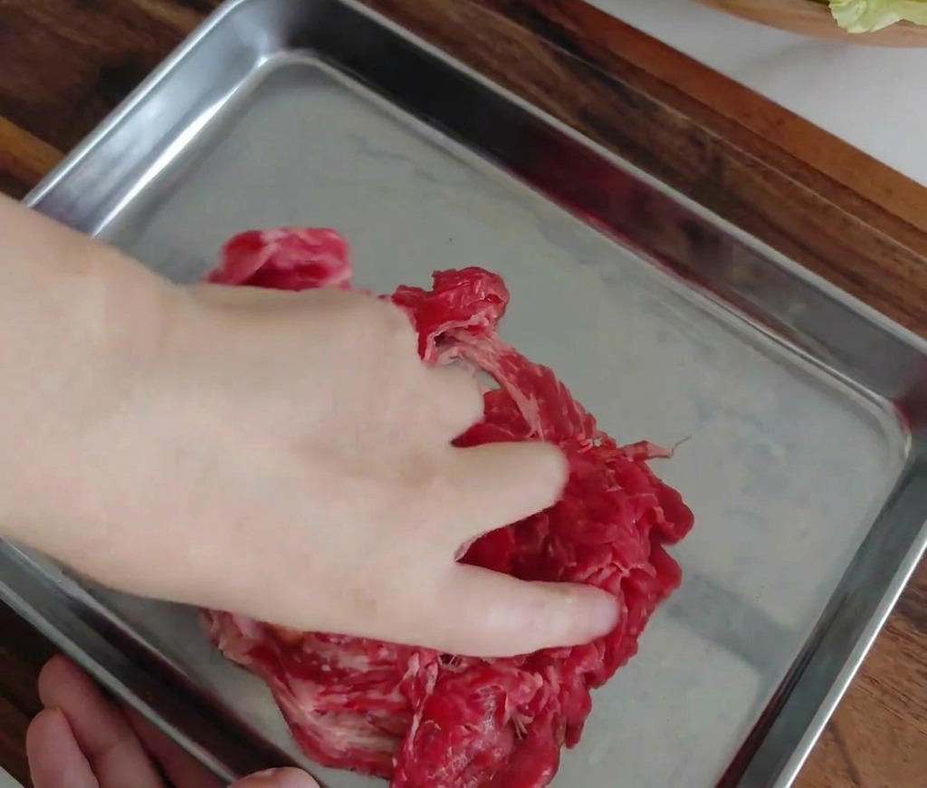 Mano che mescola il manzo marinato in un vassoio di metallo.