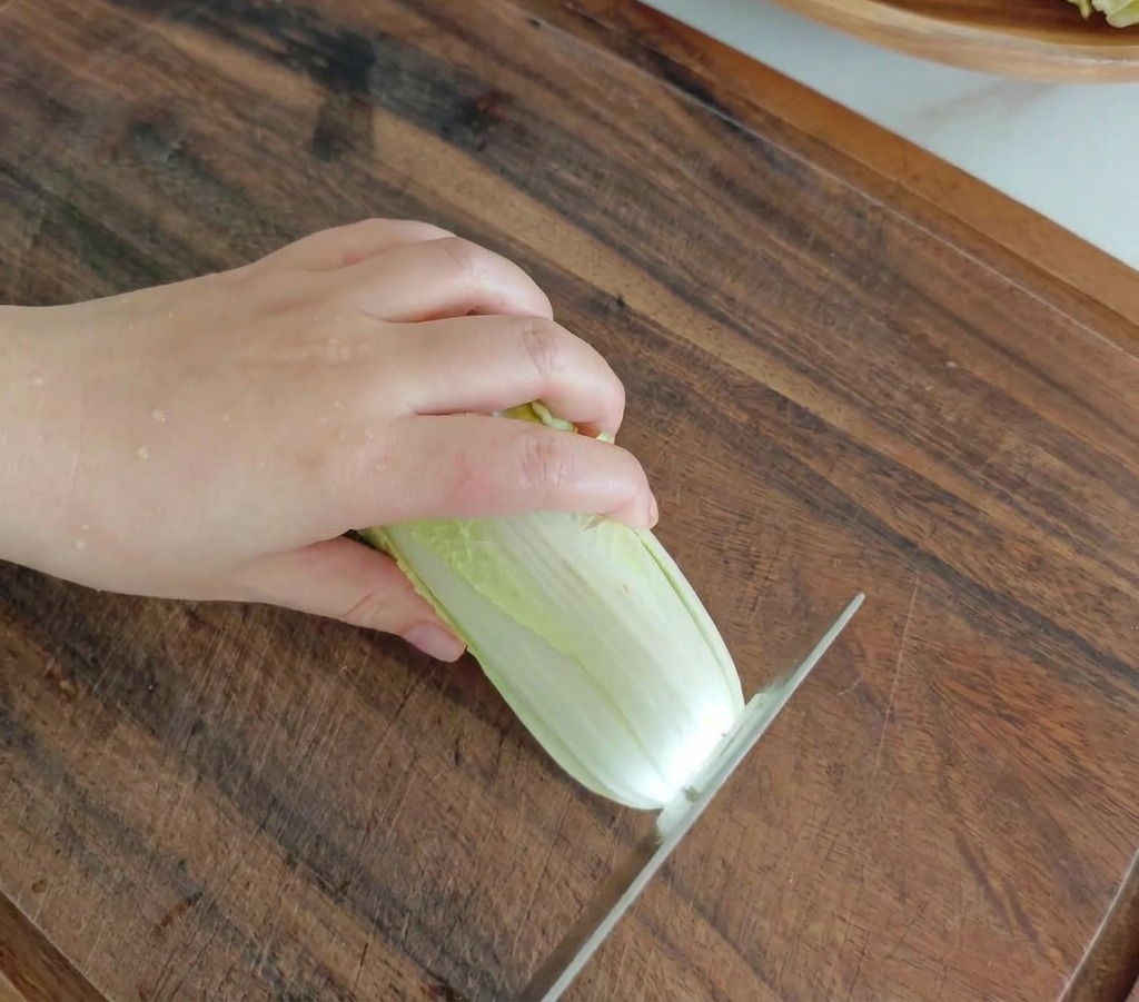 Coltello da cucina che taglia un cavolo baby su un tagliere di legno scuro.