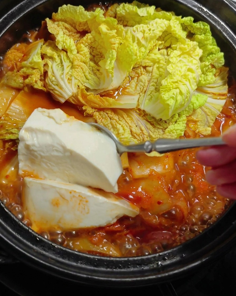 Un grosso cucchiaio di tofu bianco calato in uno stufato rosso bollente.