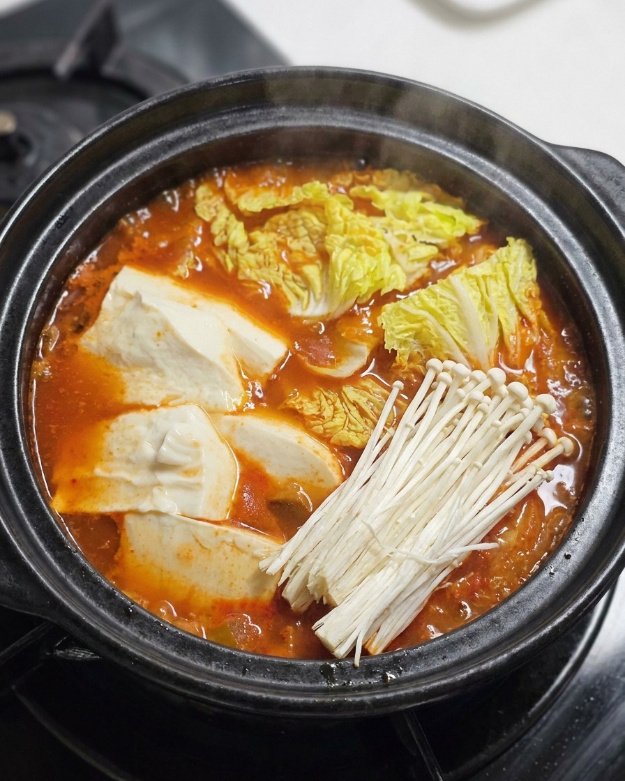 Manzo, funghi enoki e cipollotti aggiunti sopra uno stufato rosso bollente.