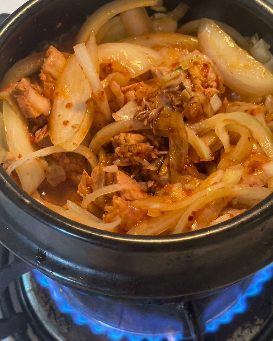 Un primo piano di salsa di soia scura versata sopra il tonno e il kimchi nella pentola di cottura.