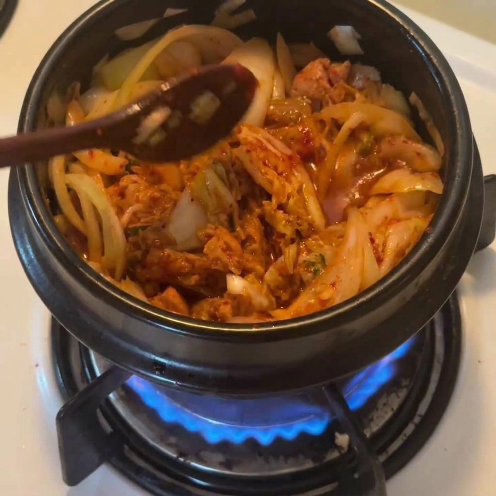 Un cucchiaio di legno che spolvera abbondante peperoncino coreano rosso sopra il composto nella pentola.