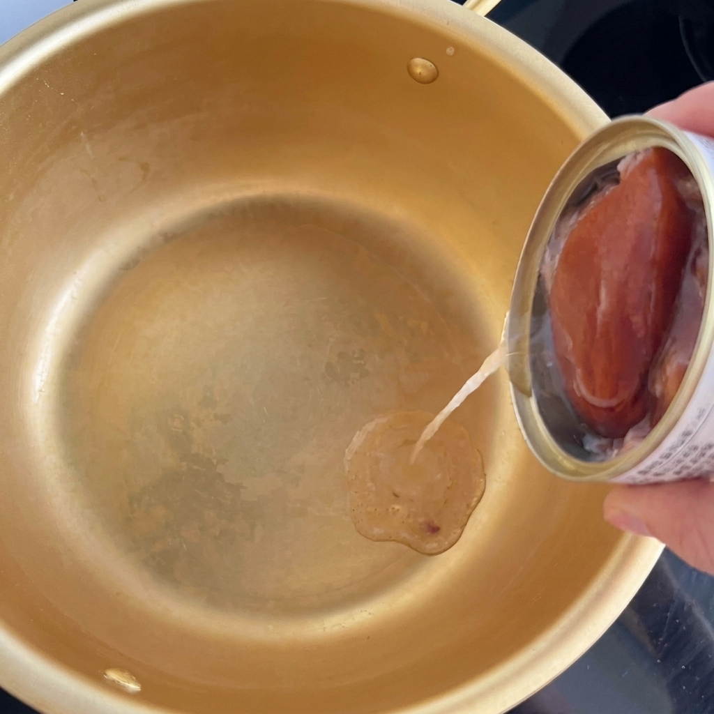 Olio versato da una scatoletta di tonno al centro di una pentola coreana dorata.