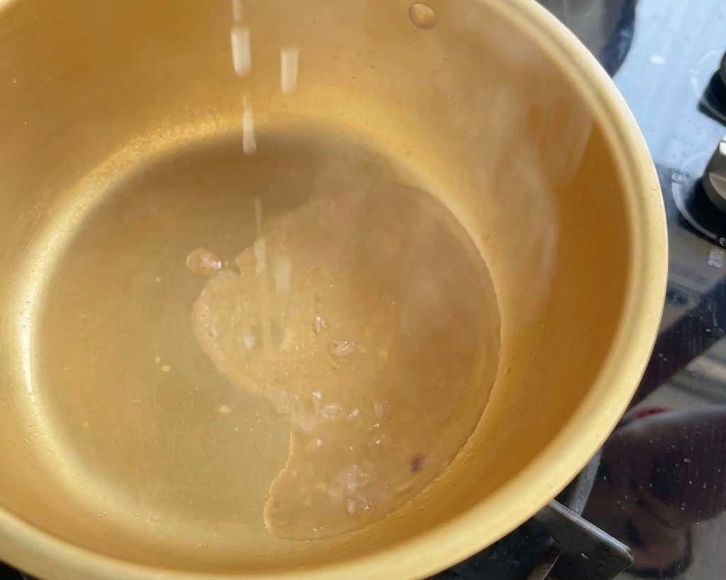 Pezzetti di cipollotto tritato che cadono in una pentola dorata fumante con olio di tonno caldo.