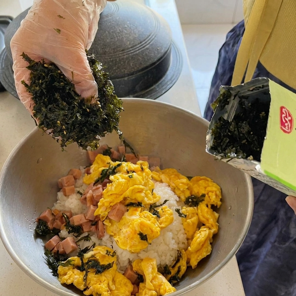 Grossi pezzi di tonno in scatola aggiunti a una zuppa di kimchi rossa e bollente in una pentola dorata.