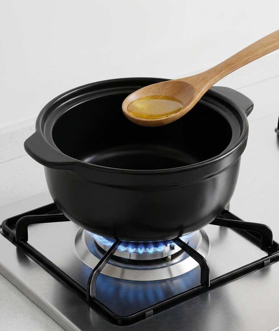 Un cucchiaio di legno versa olio di sesamo dorato sul fondo di una pentola di ceramica scura su una fiamma a gas.