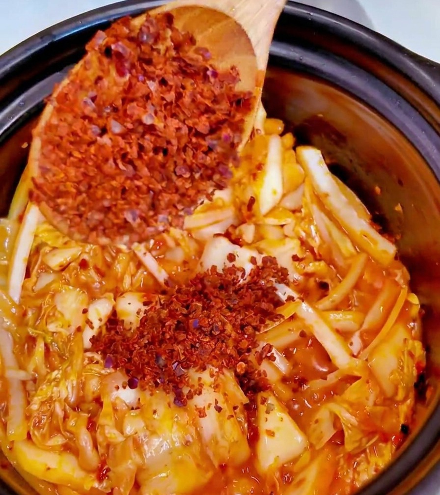 Aggiunta di un cucchiaio di polvere di peperoncino rosso fine nella pentola con il kimchi e gli odori.