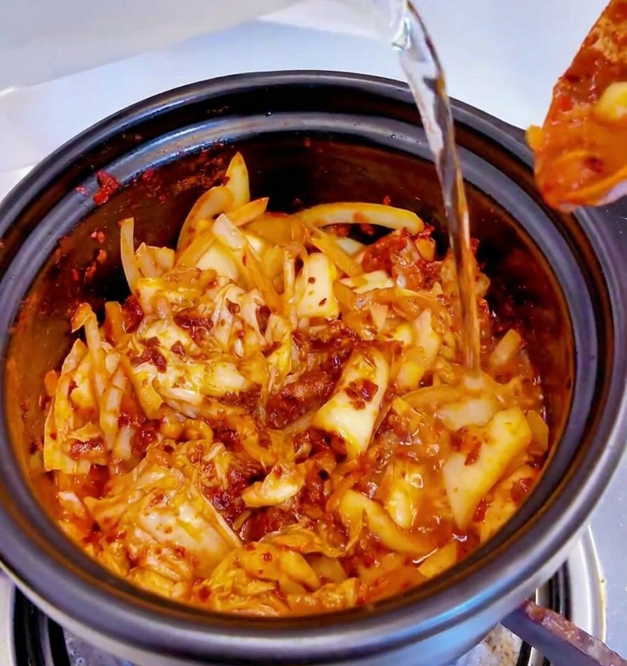 Acqua versata da un contenitore in una pentola nera piena della base piccante di kimchi.