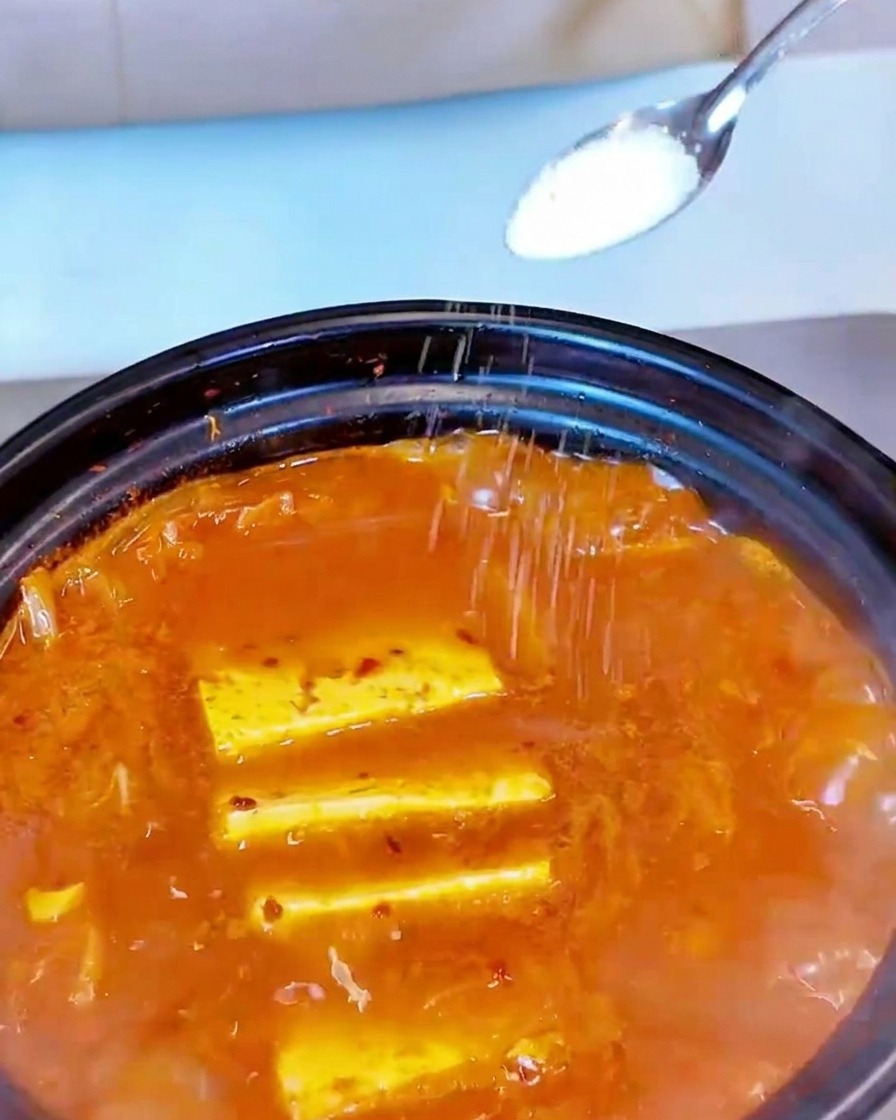 Sale bianco spolverato da un cucchiaino sulla superficie di una zuppa rossa che sobbolle.
