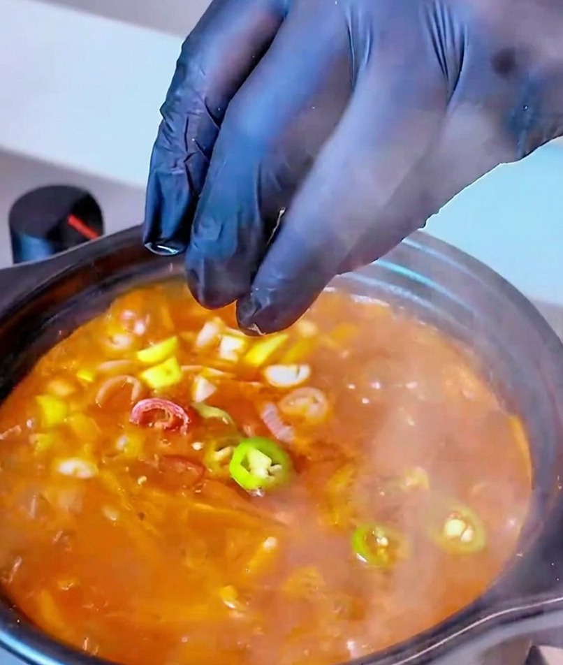 Rondelle di peperoncino rosso e verde aggiunte come guarnizione finale a una pentola bollente di Zuppa di Kimchi e Tonno.
