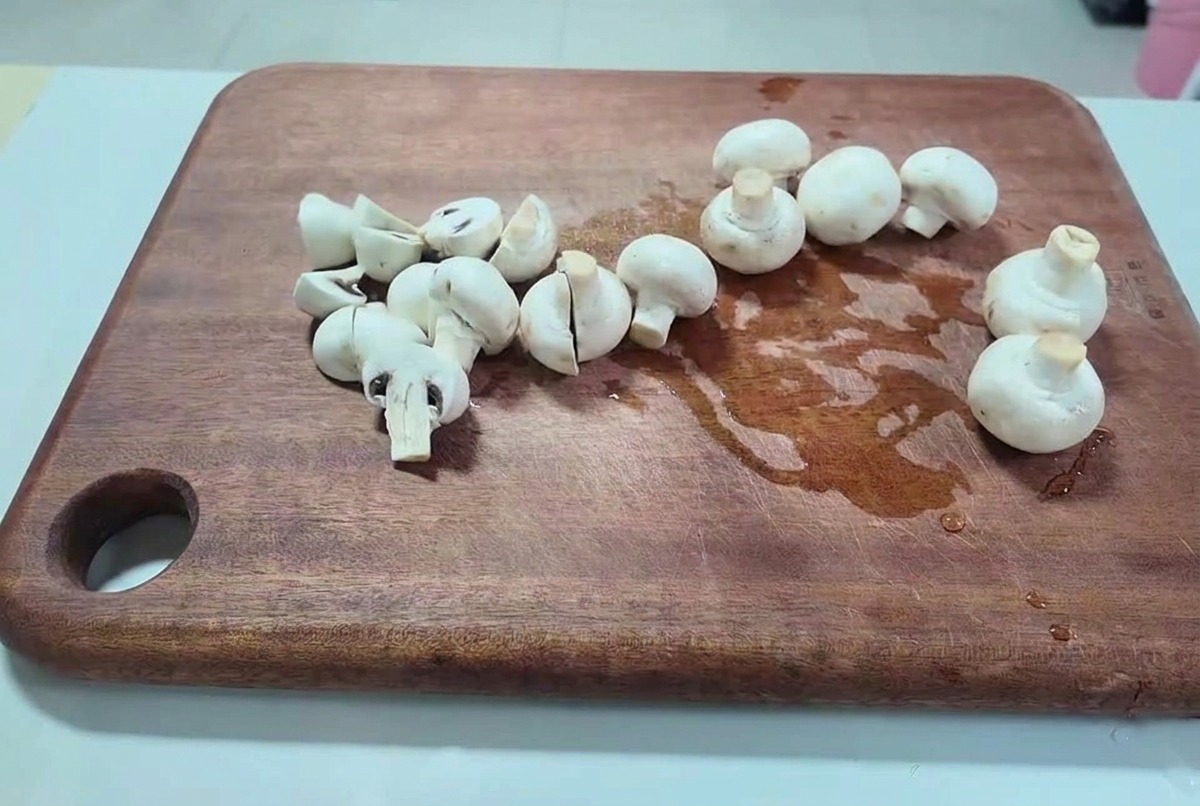 Funghi champignon bianchi freschi tagliati a metà e fette spesse su un tagliere di legno scuro.