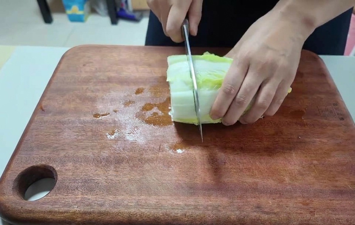 Primo piano di mani che usano un coltello da chef per tagliare foglie di cavolo cinese su un tagliere.