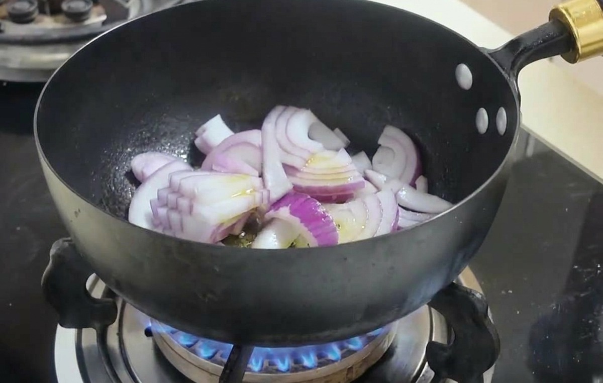 Fette di cipolla rossa saltate in un wok nero su una fiamma a gas blu.