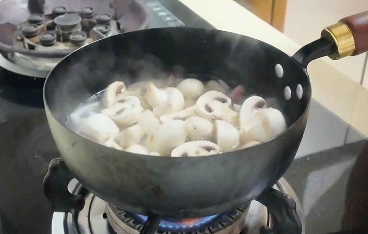 Funghi affettati e cubetti di tofu che bollono in un brodo dentro una padella scura.