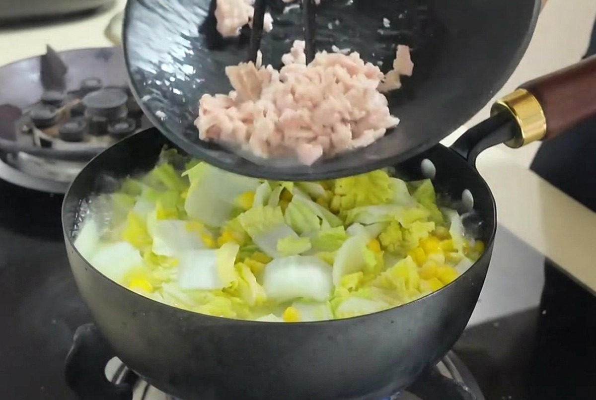 Tonno a pezzi versato da un piatto nero con le bacchette in una zuppa di verdure che bolle.