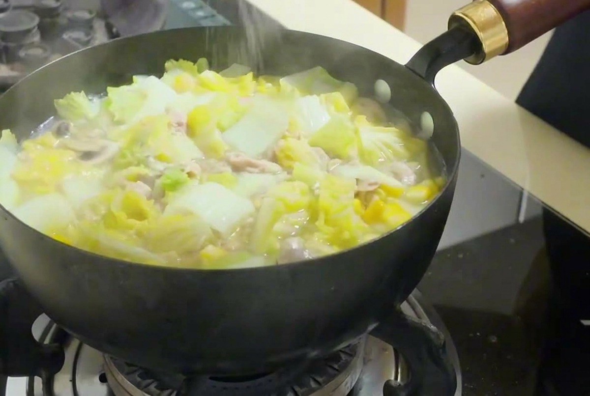 Una mano che sparge sale fino in una padella fumante con verdure, tofu e tonno.