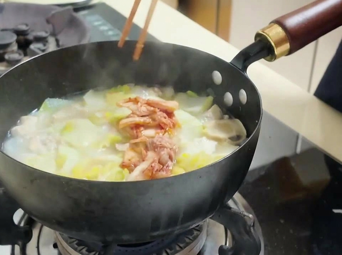 Una persona che aggiunge kimchi rosso tritato in una pentola con tofu e cavolo.
