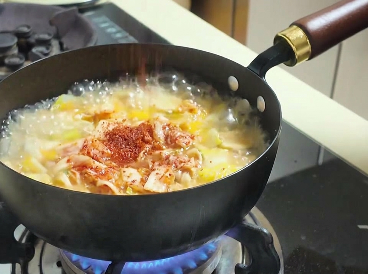 Polvere di peperoncino rosso spolverata sopra una zuppa bollente con kimchi e verdure.