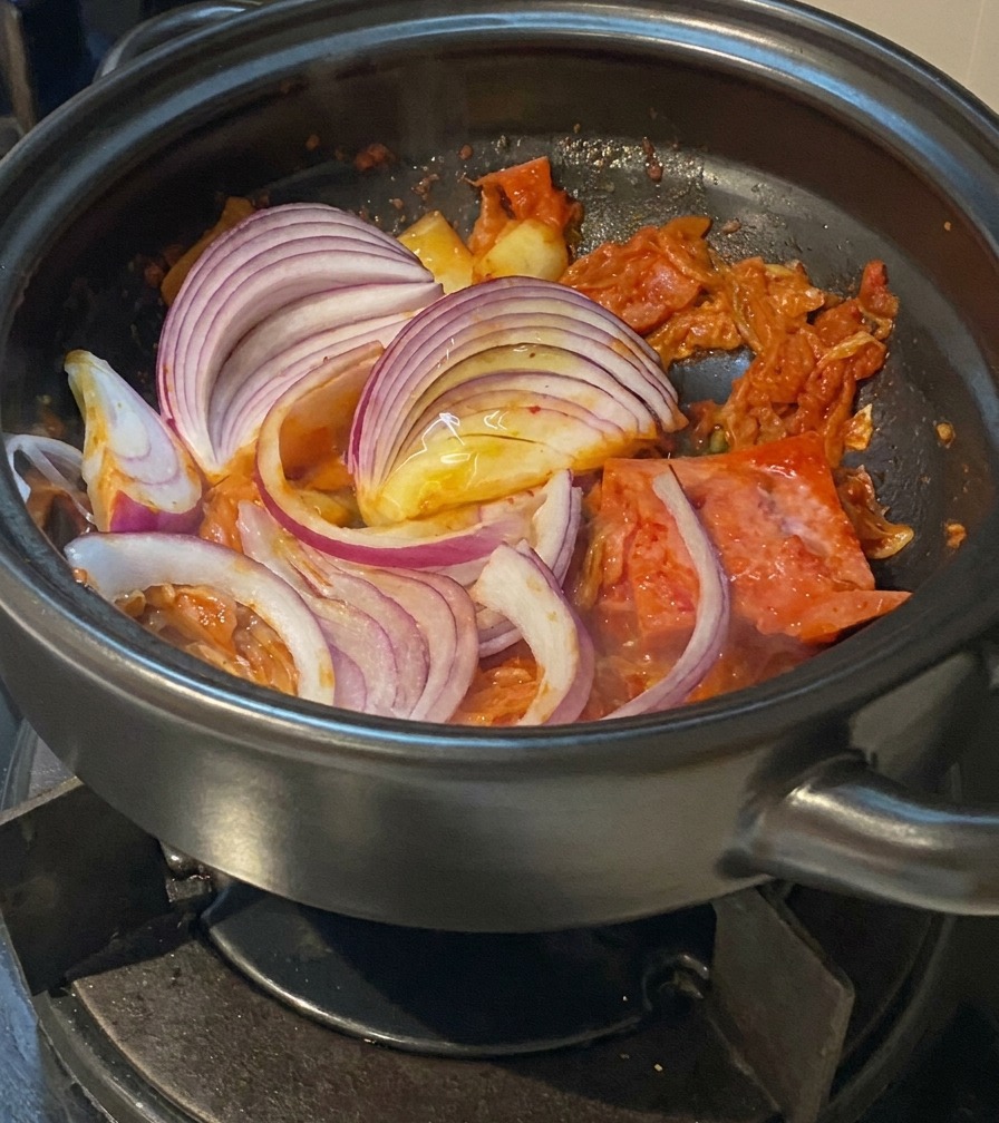 Cipolla rossa a fette aggiunta al mix di kimchi e maiale.