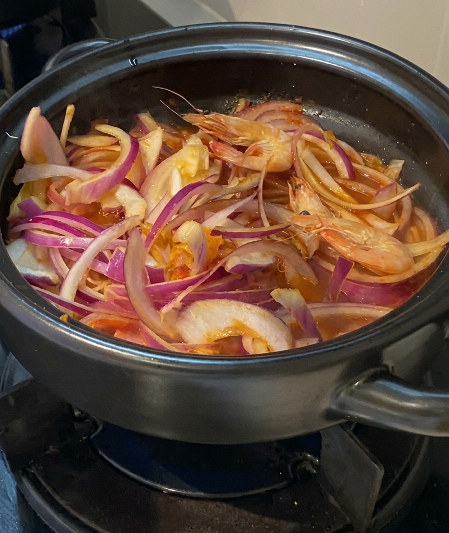 Gamberi freschi interi aggiunti agli altri ingredienti nella pentola.