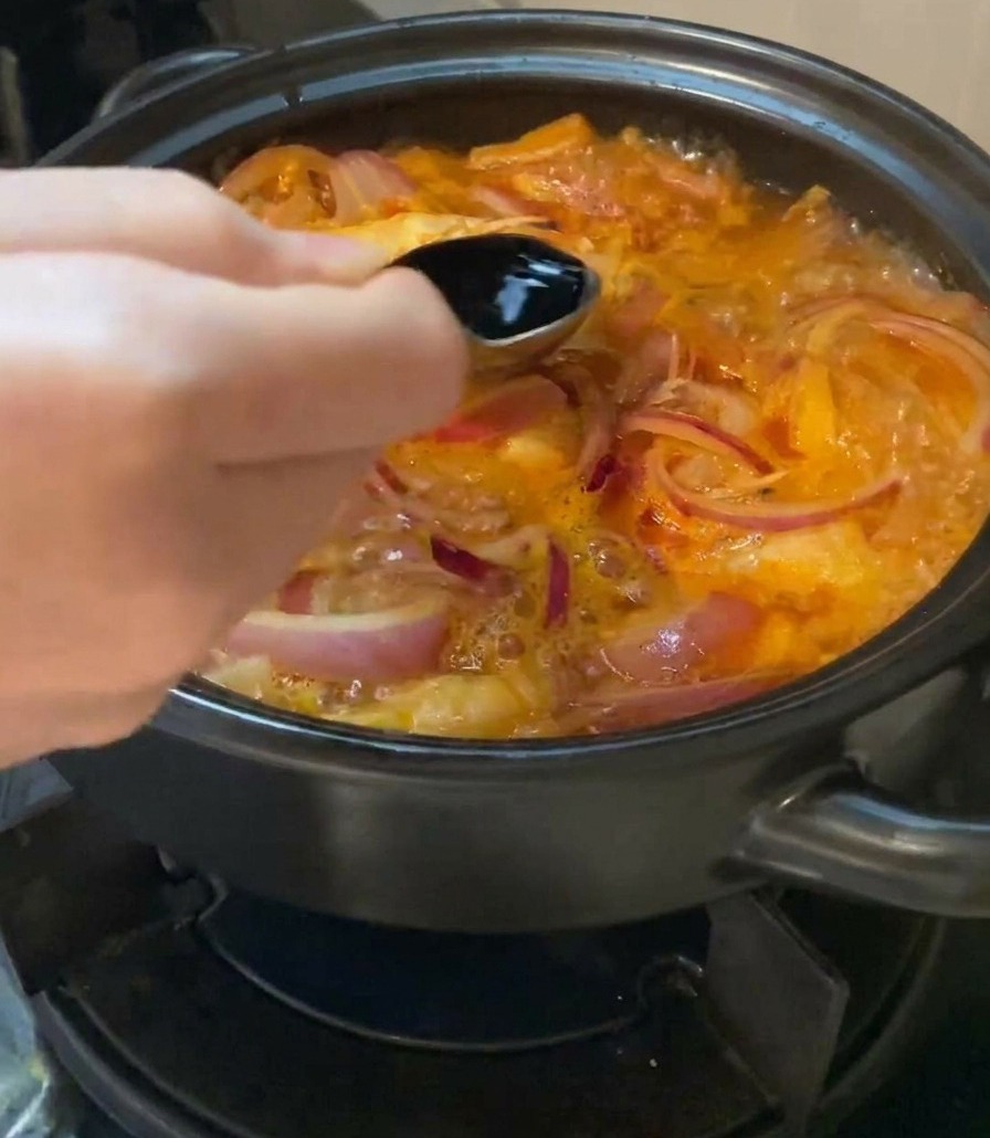 Salsa di soia chiara versata con un cucchiaio nella zuppa bollente.