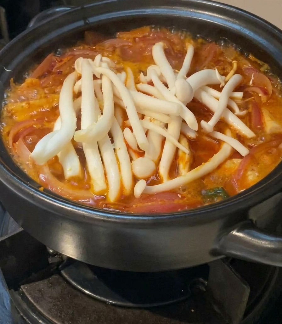 Funghi shimeji bianchi disposti sopra la zuppa rossa che sobbolle.