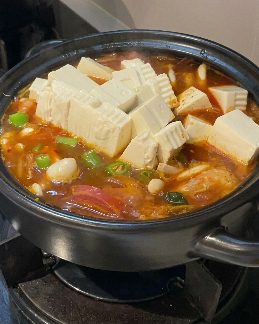 Cubetti di tofu bianco e fette di peperoncino verde aggiunti alla zuppa in ebollizione.