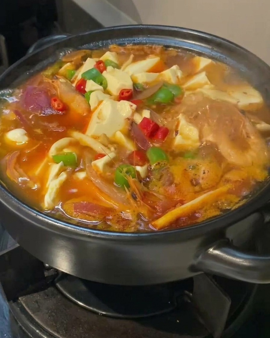 Zuppa di kimchi e tofu che sobbolle, guarnita con peperoncini rossi e verdi freschi.