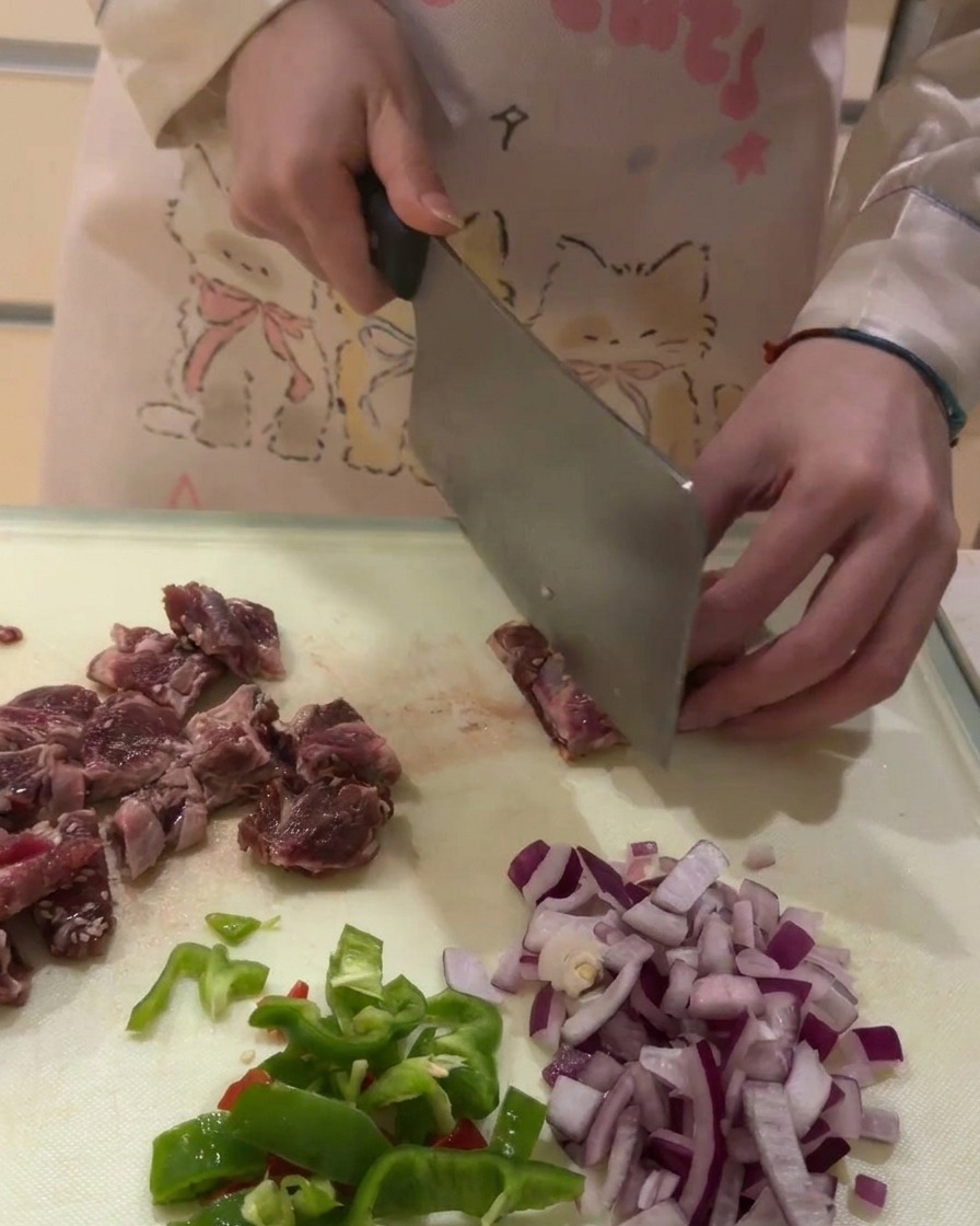 Un primo piano della carne delle costine di manzo tagliata a cubetti uniformi su un tagliere bianco.