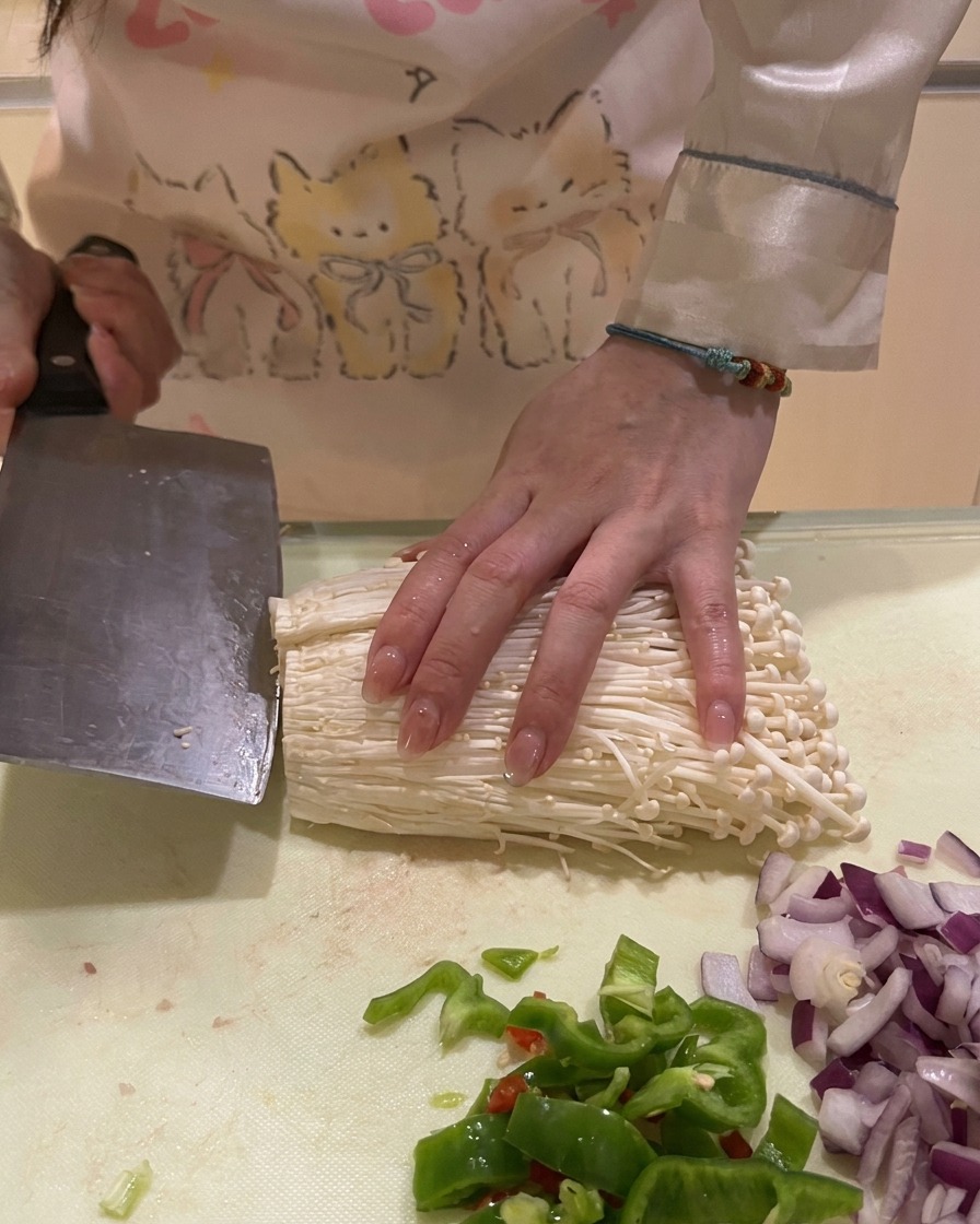 Taglio della base legnosa di un mazzetto di funghi enoki bianchi su un piano di lavoro.
