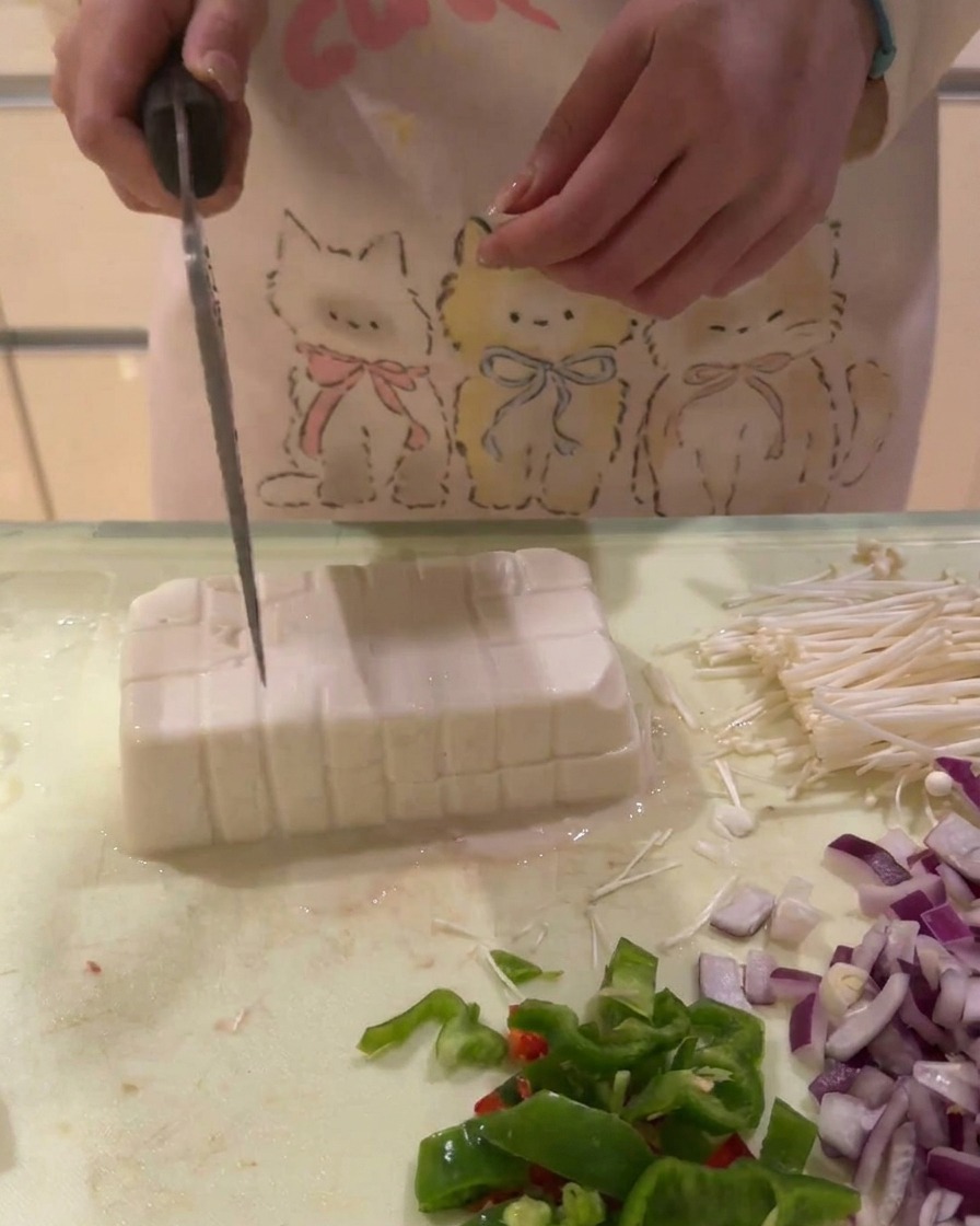 Un blocco di tofu bianco tagliato a griglia in piccoli cubetti regolari su un tagliere.