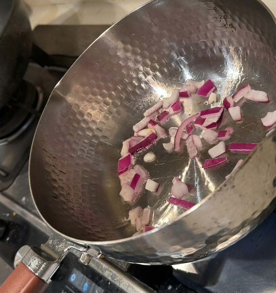 Cipolla rossa tritata che soffrigge in una pentola di metallo con un leggero velo dolio.